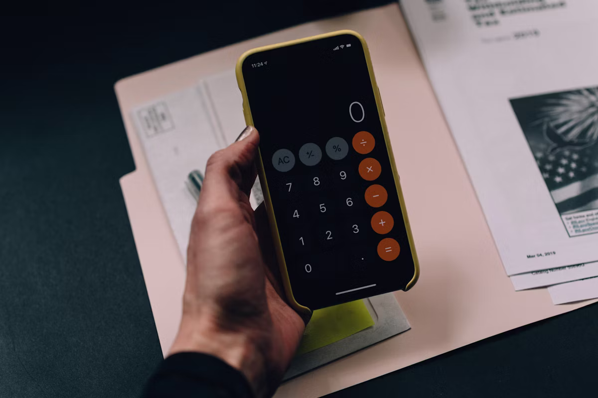 Hand holding a phone calculator over a folder of tax documents